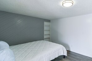 Ein Schlafzimmer mit einem Bett, einer weißen Wand, einer Holztakplattenwand und einer Deckenleuchte.