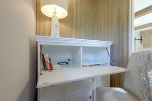 Un escritorio blanco con una lámpara, una silla y un panel de pared de madera.