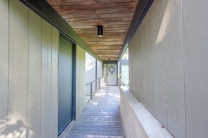 A covered walkway with a wooden ceiling, a door with a wreath, and a railing. - Mid-century Modern Chateau du Coach House (Iowa City)