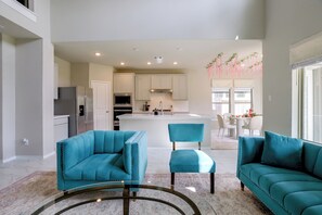 A modern kitchen with white cabinets, stainless steel appliances, and a central island. There are two teal upholstered chairs and a teal sofa in the living area. - Richmond Home 12 Mi to Cinco Ranch Lakes (Richmond)