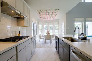 A modern kitchen with a central island, a dining area with a table and chairs, and a view of the outdoors through large windows. - Richmond Home 12 Mi to Cinco Ranch Lakes (Richmond)