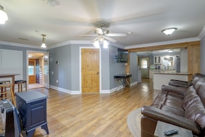A spacious living area with a brown leather sofa, a wood-burning stove, and a ceiling fan. - Bayou Days, Fire Pit Nights! Denham Springs Home (Denham Springs)