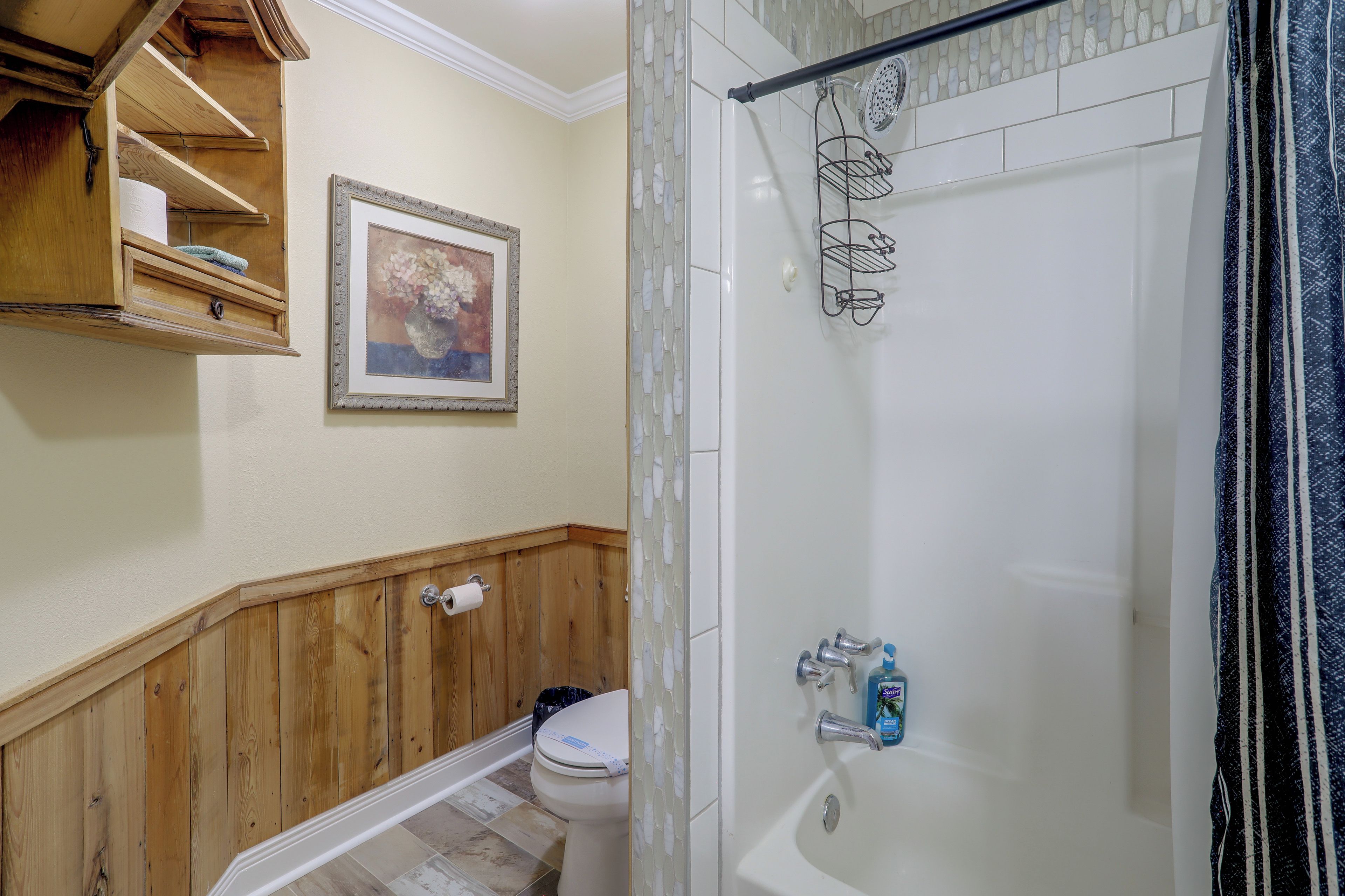A bathroom with a shower, toilet, and a wooden vanity with shelves.