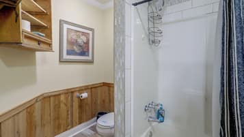 A bathroom with a shower, toilet, and a wooden vanity with shelves.