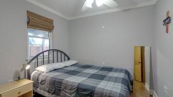 A bedroom with a bed, a nightstand, a lamp, a window with a view, a ceiling fan, and a door.