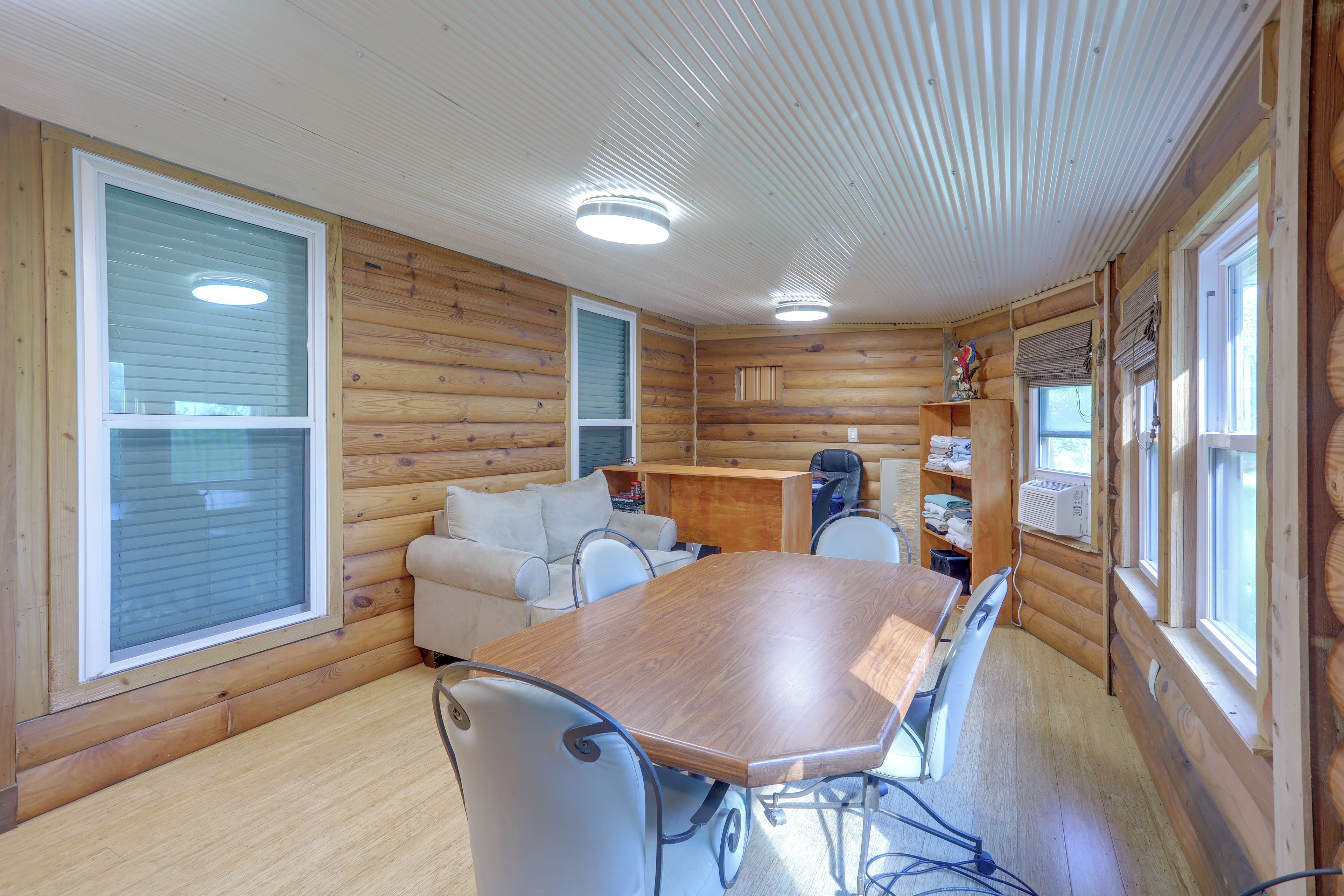 A cabin interior with a wooden dining table, two chairs, a sofa, and a small kitchenette area.