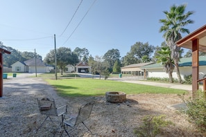A residential area with a gravel driveway, a metal bench, a stone fire pit, and houses with green roofs.