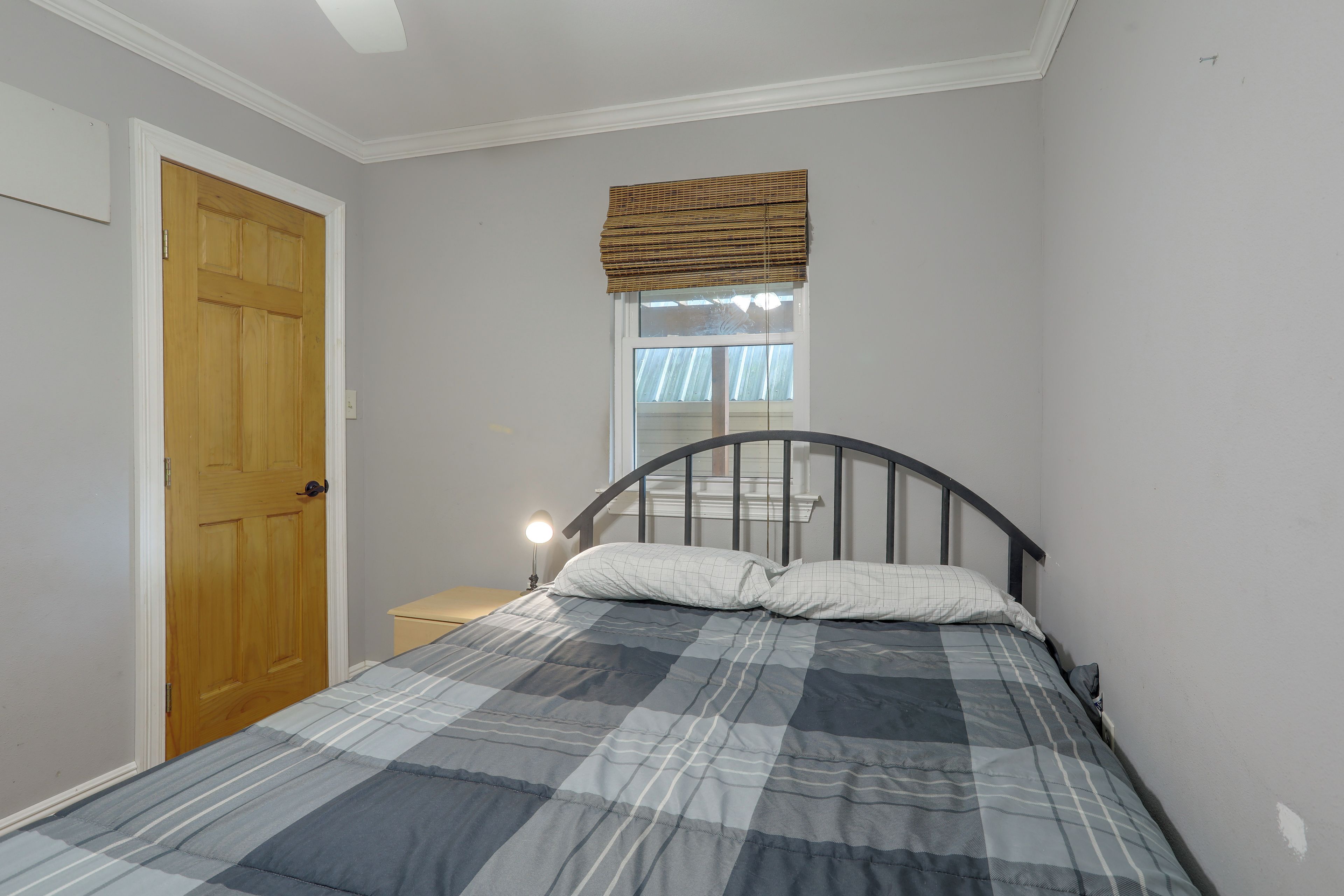 A bedroom with a bed, a wooden door, a nightstand, and a window with blinds.