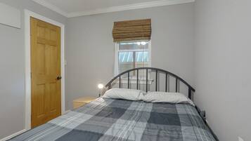 A bedroom with a bed, a wooden door, a nightstand, and a window with blinds.
