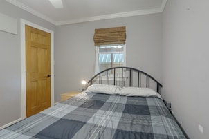 A bedroom with a bed, a wooden door, a nightstand, and a window with blinds.