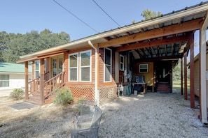 A wooden cabin with a covered porch, a gravel driveway, and a metal chair. - Bayou Days, Fire Pit Nights! Denham Springs Home (Denham Springs)