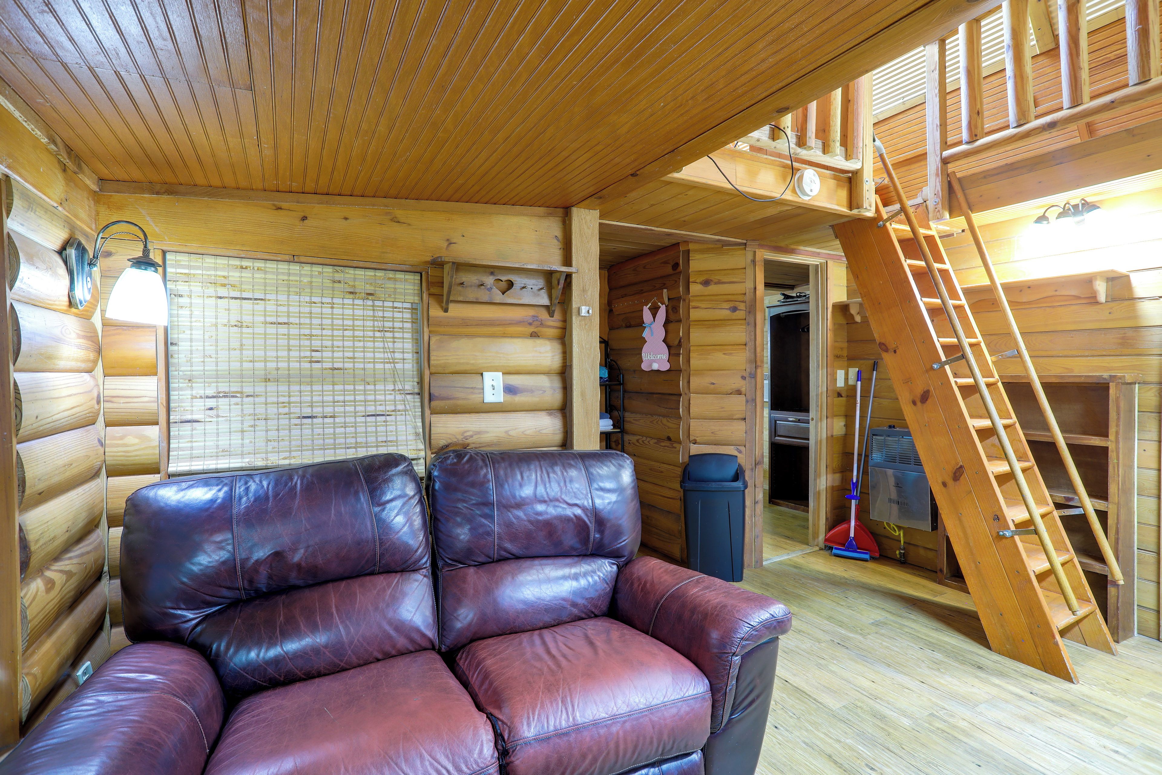 A log cabin interior with a leather sofa, a ladder, and a wooden ceiling.