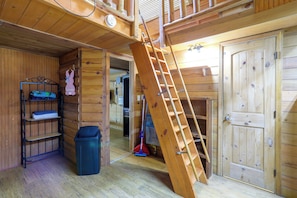 A wooden interior with a ladder leading to an upper level, a metal shelf unit, and a door.