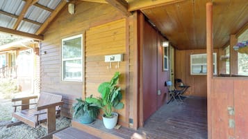 A wooden cabin with a porch, a bench, and potted plants.