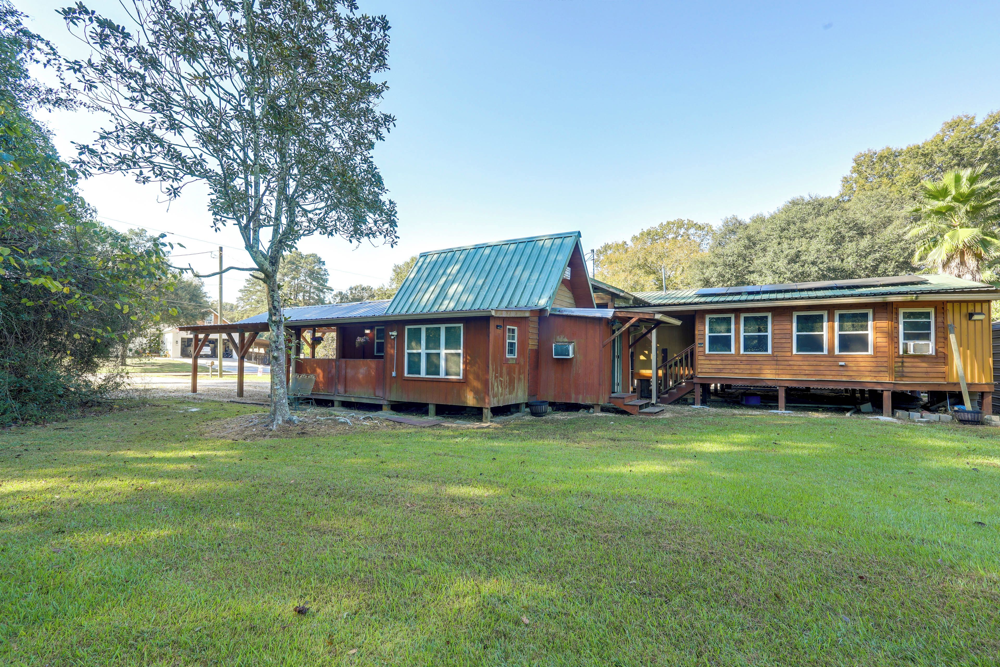 A two-story wooden house with a metal roof, surrounded by a grassy yard and trees.