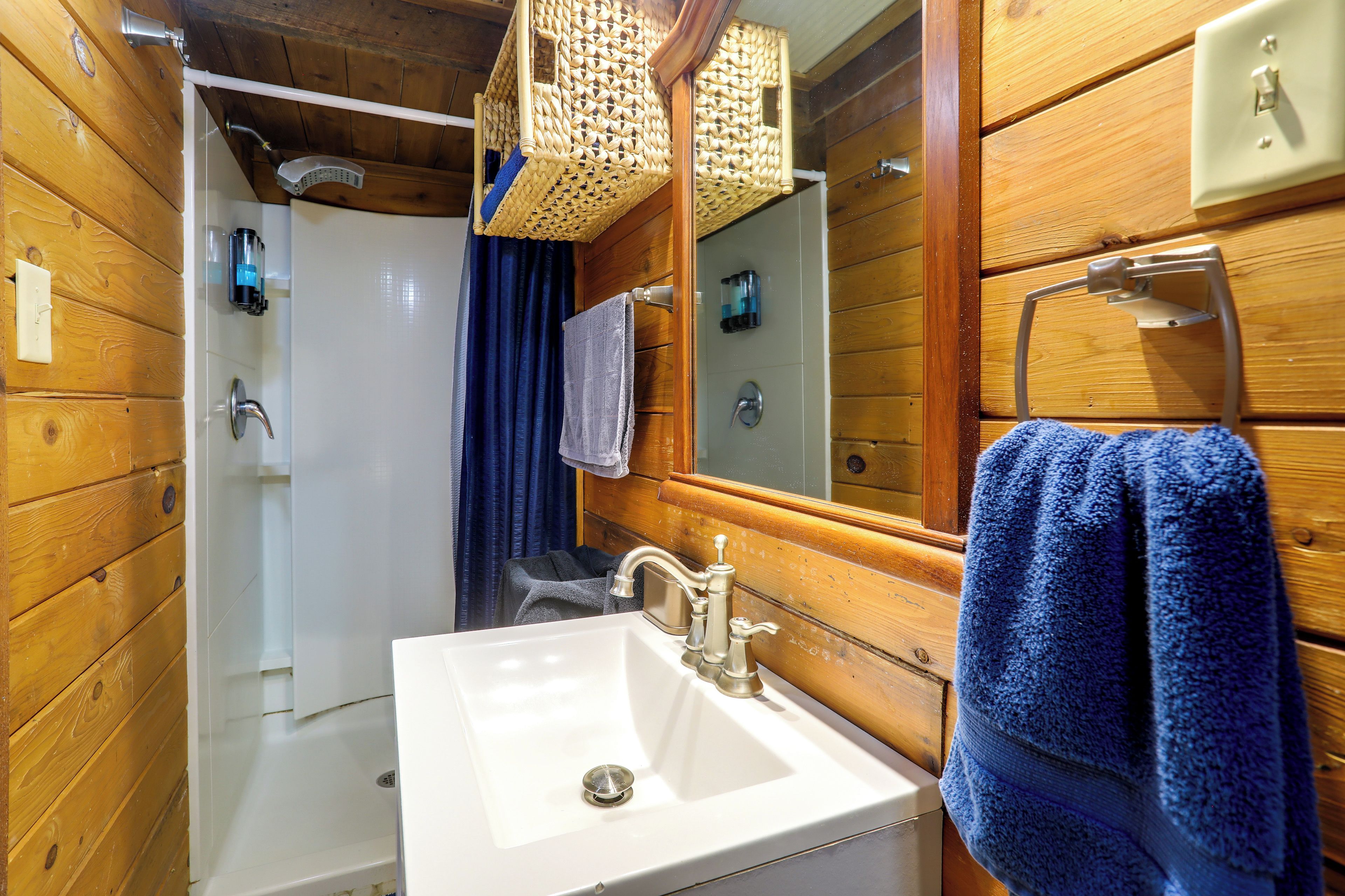 A wooden bathroom with a white sink, a mirror, a towel rack, and a shower area.