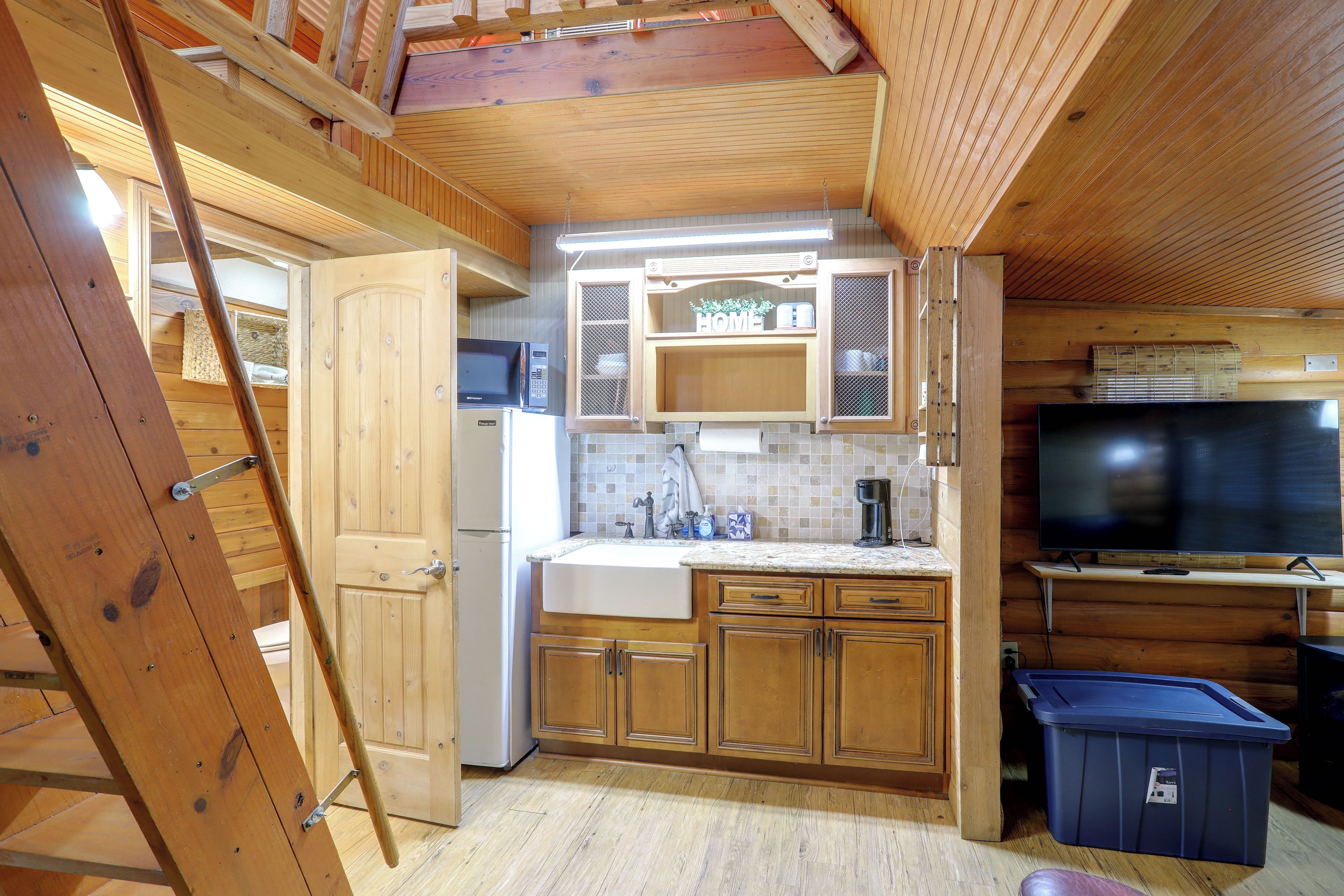 A compact kitchen with wooden cabinets, a microwave, a sink, and a television.