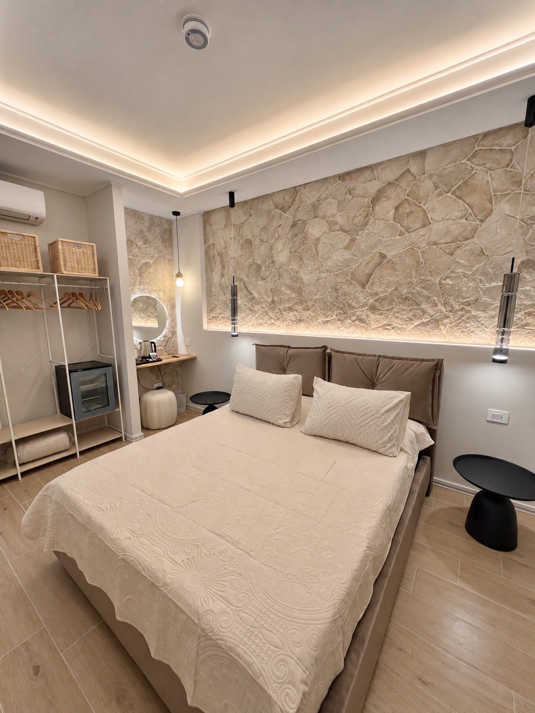 Ein modernes Schlafzimmer mit einem großen Bett, einer Wand aus Stein, einem integrierten Fernseher und einem Nachttisch.