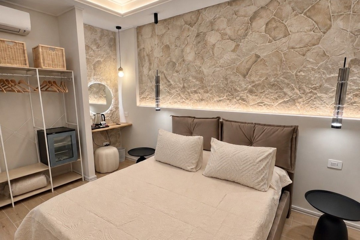 Een moderne slaapkamer met een groot bed, een accentmuur van steen, een ingebouwde televisie en een nachtkastje.