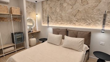 Ein modernes Schlafzimmer mit einem großen Bett, einer Wand aus Stein, einem integrierten Fernseher und einem Nachttisch.