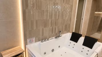 Ein modernes Badezimmer mit einer großen weißen Badewanne, einem hölzernen Nachttisch und einer gefliesten Wand mit einem einzigartigen Muster.