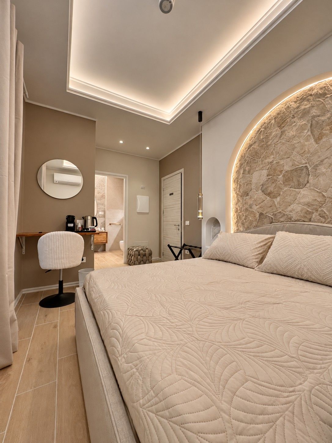 Ein modernes Schlafzimmer mit einem großen Bett, einem runden Spiegel, einer Kaffeestation und einer Wand mit Steinakzenten.