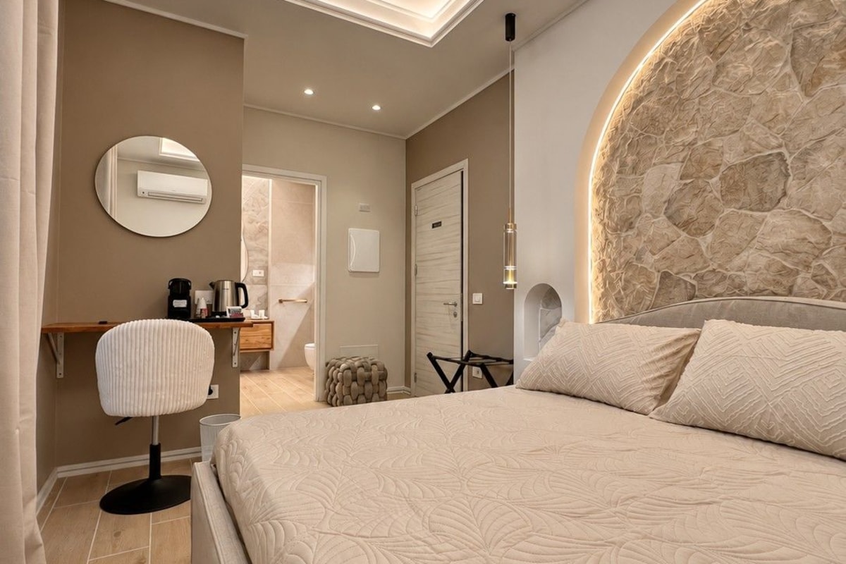 Een moderne slaapkamer met een groot bed, een ronde spiegel, een koffiehoek en een accentmuur van steen.