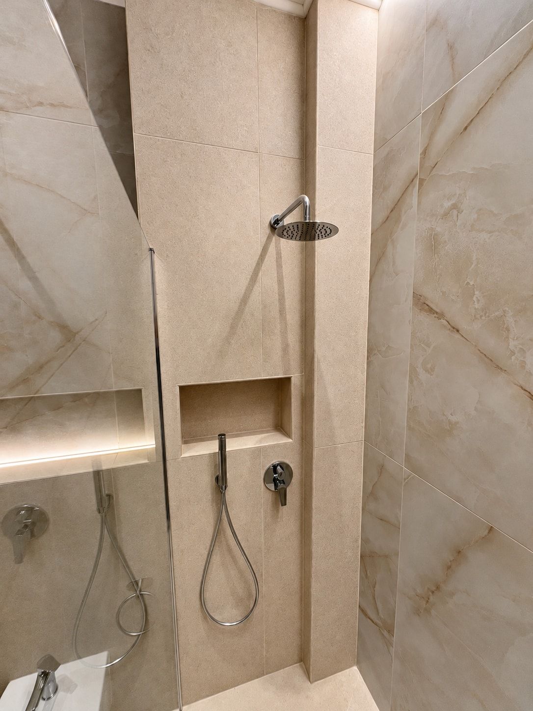 A modern bathroom with a shower enclosure, a glass door, and a built-in shelf.