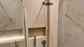 A modern bathroom with a shower enclosure, a glass door, and a built-in shelf.
