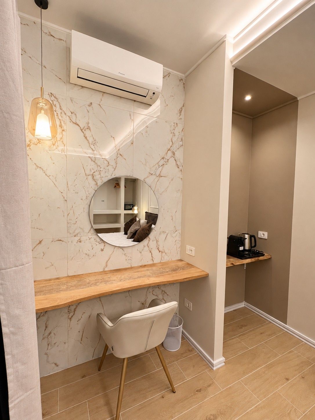 A modern bathroom with a marble wall, a round mirror, a wooden vanity, a white chair, and an air conditioning unit.