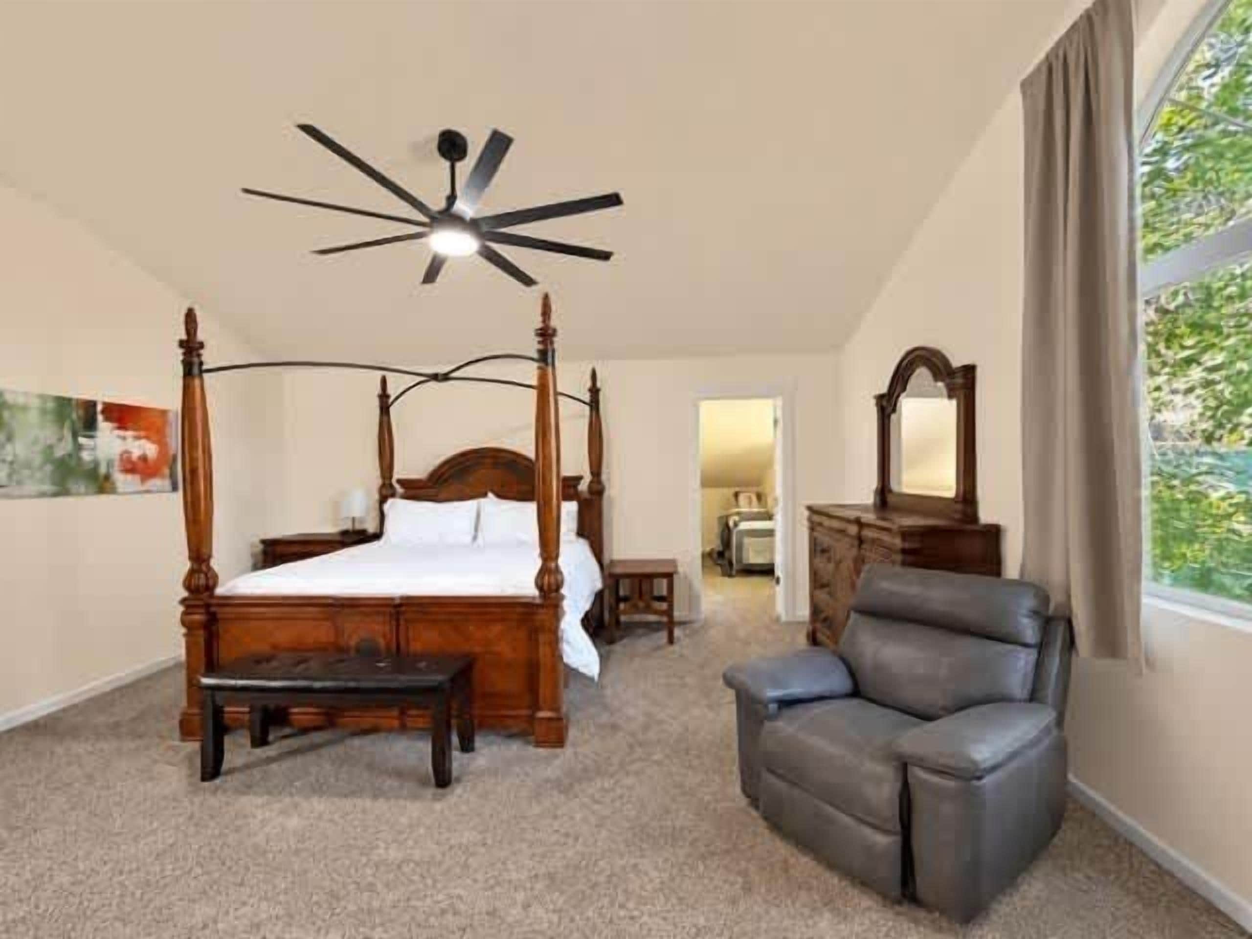 Quarto com cama de dossel, ventilador de teto, cadeira e cômoda.