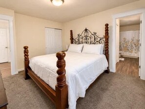 A bedroom with a wooden four-poster bed, carpeted floor, and white walls. - Spacious Midtown Home Walk to Lake Downtown (Coeur d'Alene)