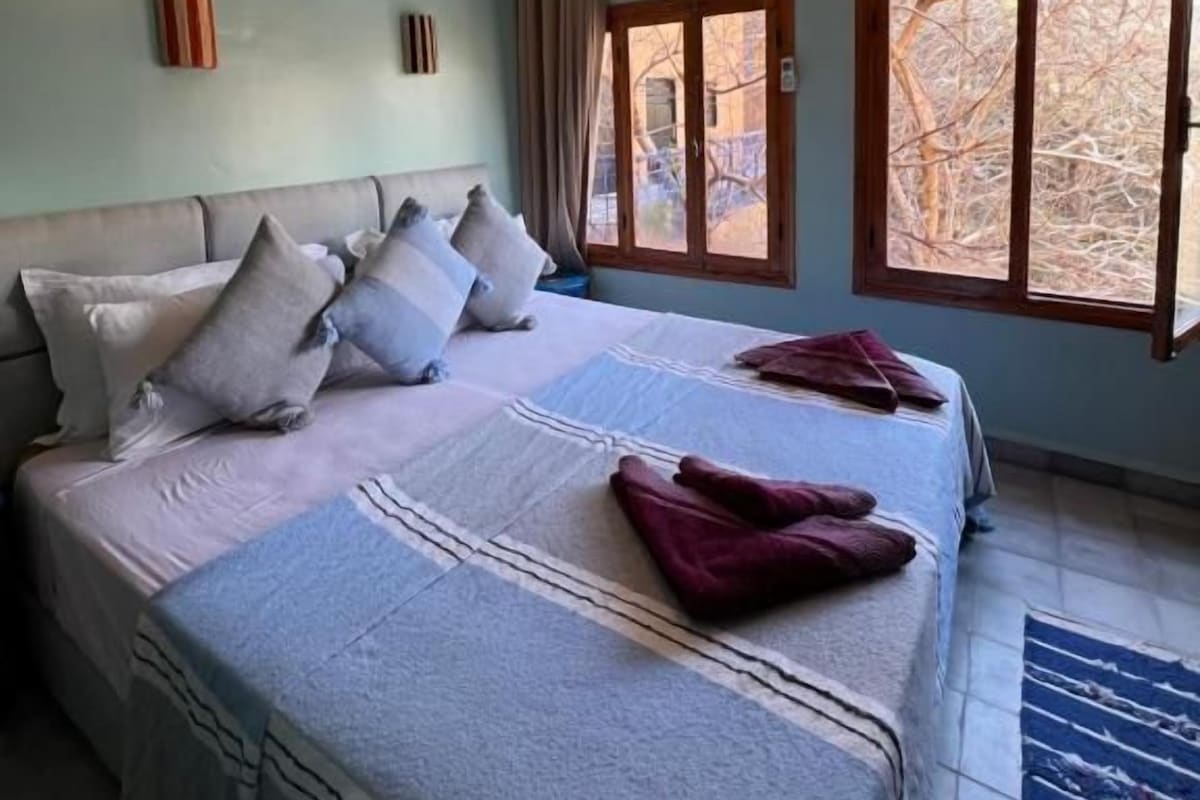 A hotel room with a large bed, a ceiling light fixture, and a window with curtains.