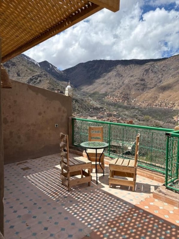 A balcony with a view of a mountainous landscape, a table with chairs, and a green railing. - La Perle De Neige (Imlil)