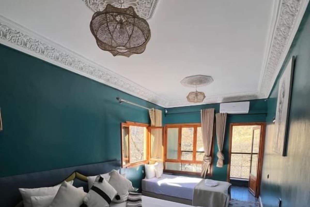 A hotel room with a large bed, a smaller bed, a window with curtains, and a decorative ceiling light.