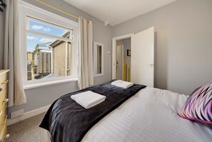 Ein Schlafzimmer mit Bett, Fenster, Tür und Blick ins Freie.
