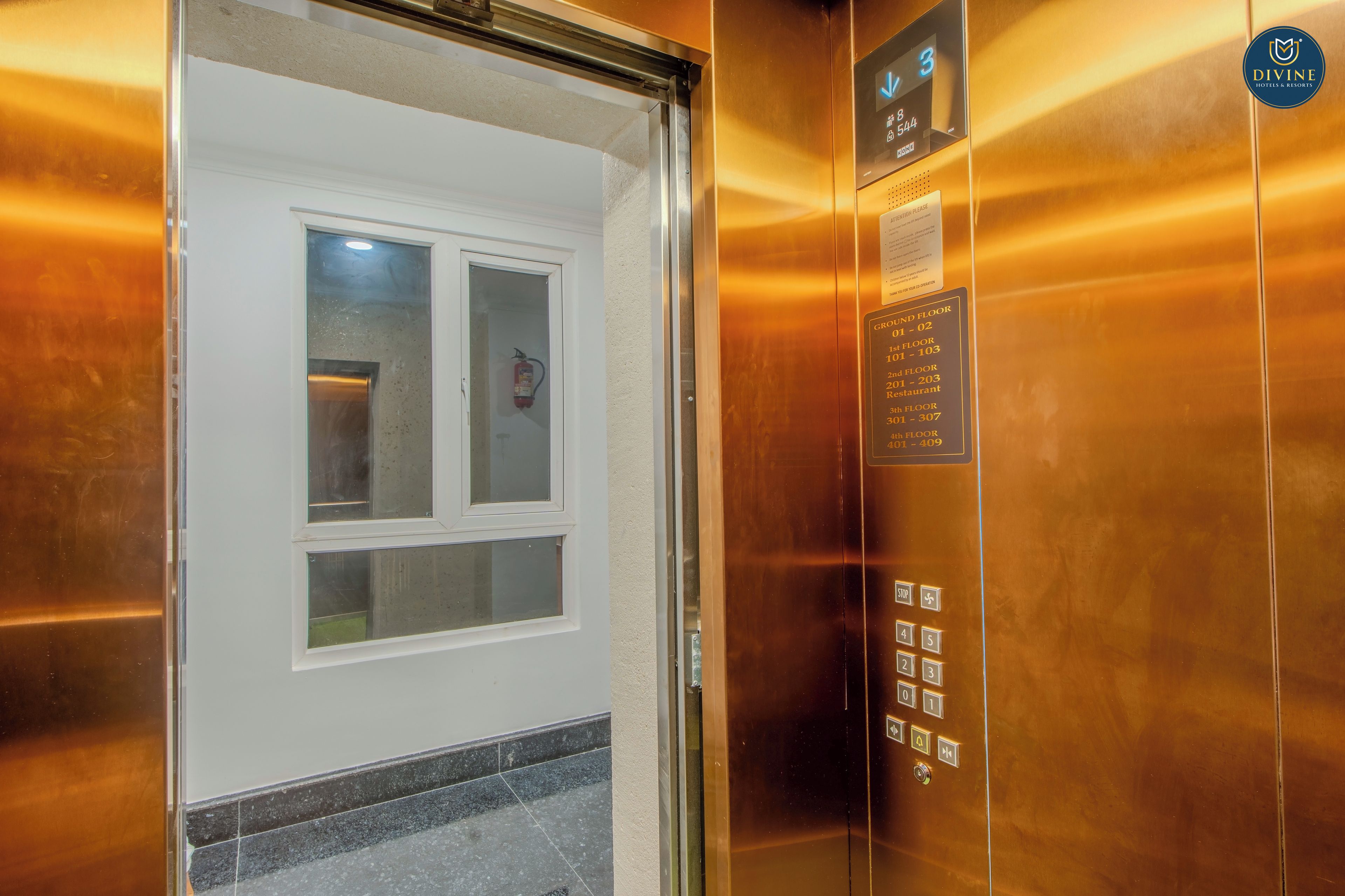 An elevator interior with a fire extinguisher mounted on the wall, a digital display with floor numbers, and a 'Group Floor' sign indicating the ground floor.