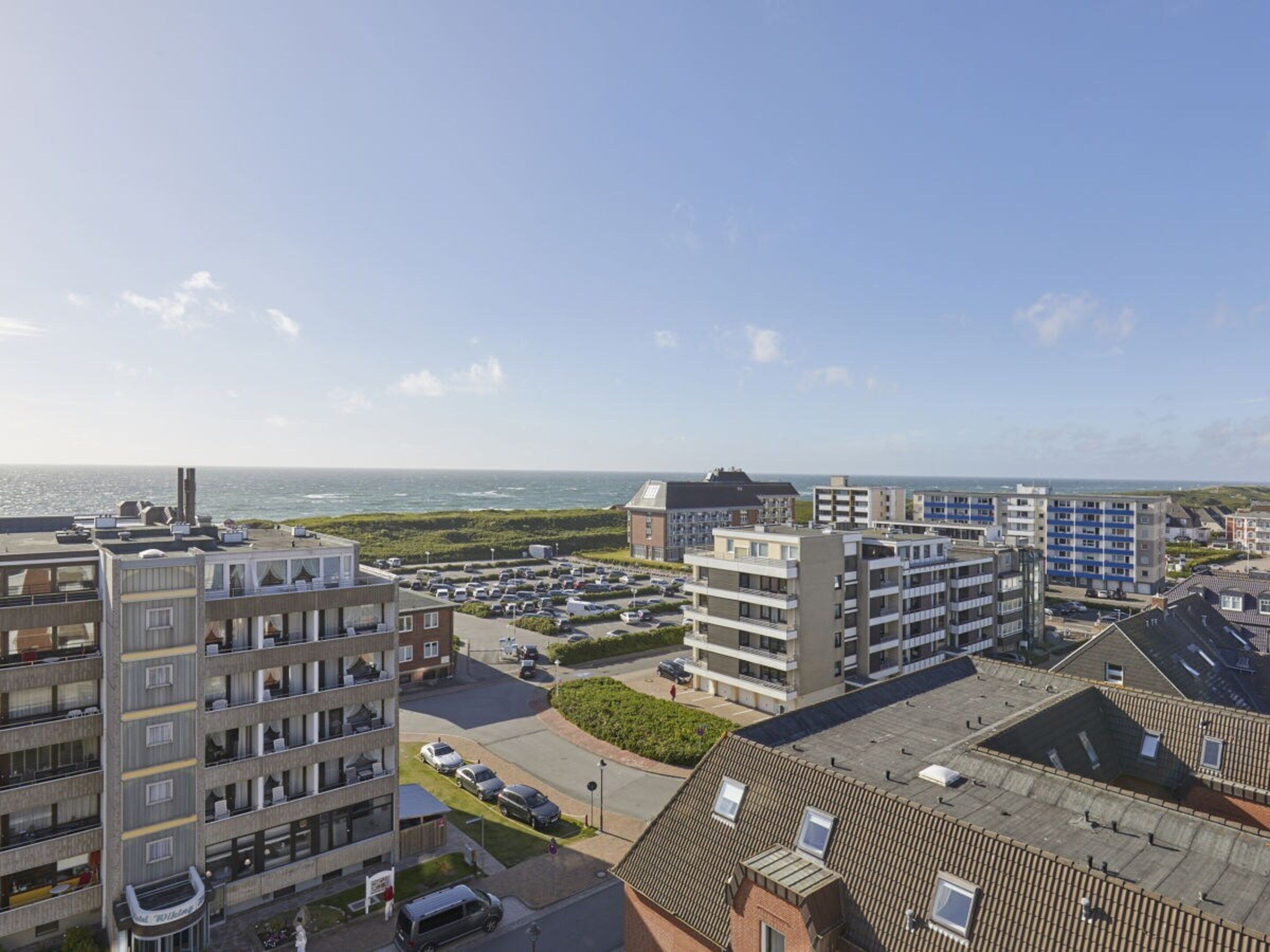 A coastal residential area with multi-story buildings, a parking lot, and a view of the sea.