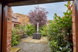 A garden pathway leading to a seating area with a table and chairs, surrounded by lush greenery and a brick wall. - Host Stay - Ruby s Retreat (York)