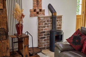 A rustic room with a brick fireplace, a wooden table with a vase, and a leather sofa. - Host Stay - Ruby s Retreat (York)