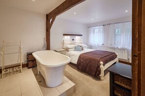 Ein Schlafzimmer mit einer großen Badewanne, einem Bett mit brauner Decke, einem Nachttisch und einem Fenster mit transparenten Vorhängen.
