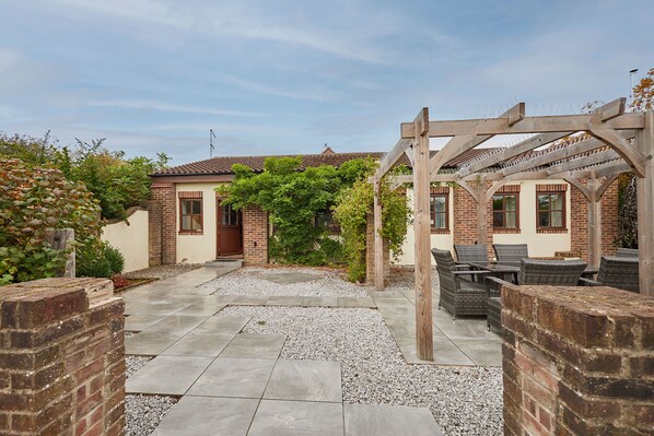 A courtyard with a pergola, outdoor seating, and a brick building with a tiled roof. - Host Stay - Bricknell Barn (York)