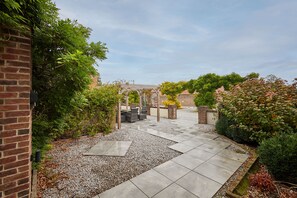 Ein gepflasterter Patio-Bereich mit einer Pergola, Sitzgelegenheiten und einem Kiesweg.