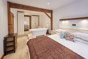 A bedroom with a large bed, a wooden ceiling beam, a white dresser, and a bathroom visible through an open door. - Host Stay - Bricknell Barn (York)