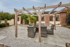An outdoor patio with a pergola, wicker furniture, and a gravel ground. - Host Stay - Bricknell Barn (York)