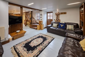 A living room with a leather sofa, a wooden coffee table, a TV, and a staircase leading to another level. - Host Stay - Ethel s Escape (York)