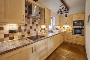 A modern kitchen with a checkered backsplash, stainless steel appliances, and wooden cabinetry. - Host Stay - Clover Leaf Cottage (York)