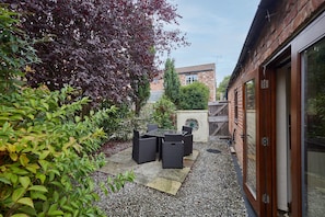A patio area with outdoor furniture, a gravel path, and a brick building with a glass door. - Host Stay - Clover Leaf Cottage (York)