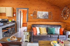 A cozy cabin interior with a wooden interior, a dining area, a living room with a leather sofa, and a kitchen with a stove and stools. - Starlight Summit Big Buck Hunter Arcade Hot Tub (Sevierville)