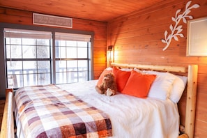 A wooden cabin room with a bed, a quilt, and a window with blinds. - Starlight Summit Big Buck Hunter Arcade Hot Tub (Sevierville)